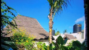 Ein tropisches Resort mit einem strohgedeckten Gebäude, einer Palme, einem Swimmingpool und einem Wassertank.