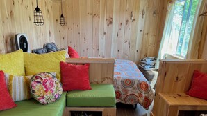 A cozy cabin interior with wooden walls, a green sofa, a wooden table, and a bed with patterned bedding. - Fun Mountain Getaway with views and WIFI. Close to Mountains, Rivers and Lakes! (Wentworth)