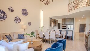A spacious living room with a sofa set, a dining area with chairs, and a kitchen in the background.