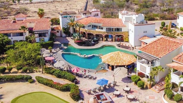 A resort with a central swimming pool, multiple guest villas, and a landscaped outdoor area with lounge chairs and umbrellas.