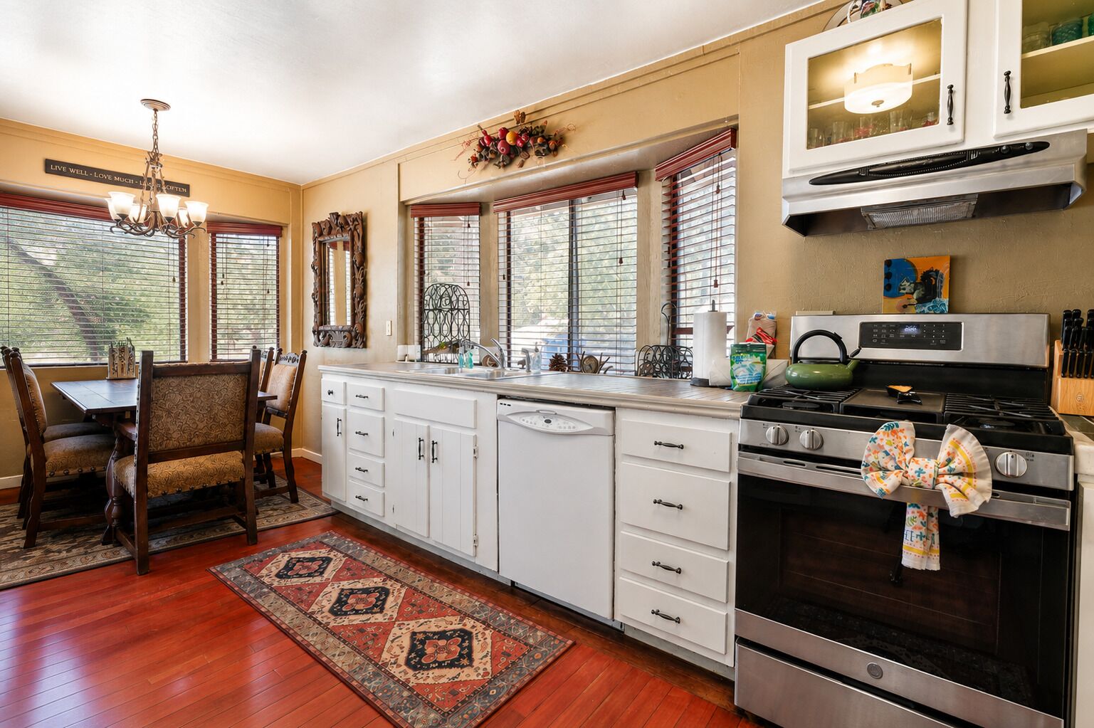 A kitchen with a dining area, wooden flooring, white cabinetry, a stove, and a chandelier.