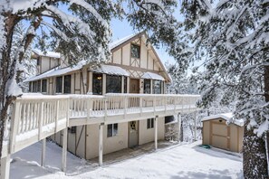 Un chalet de dos pisos con balcón, rodeado de árboles cubiertos de nieve.