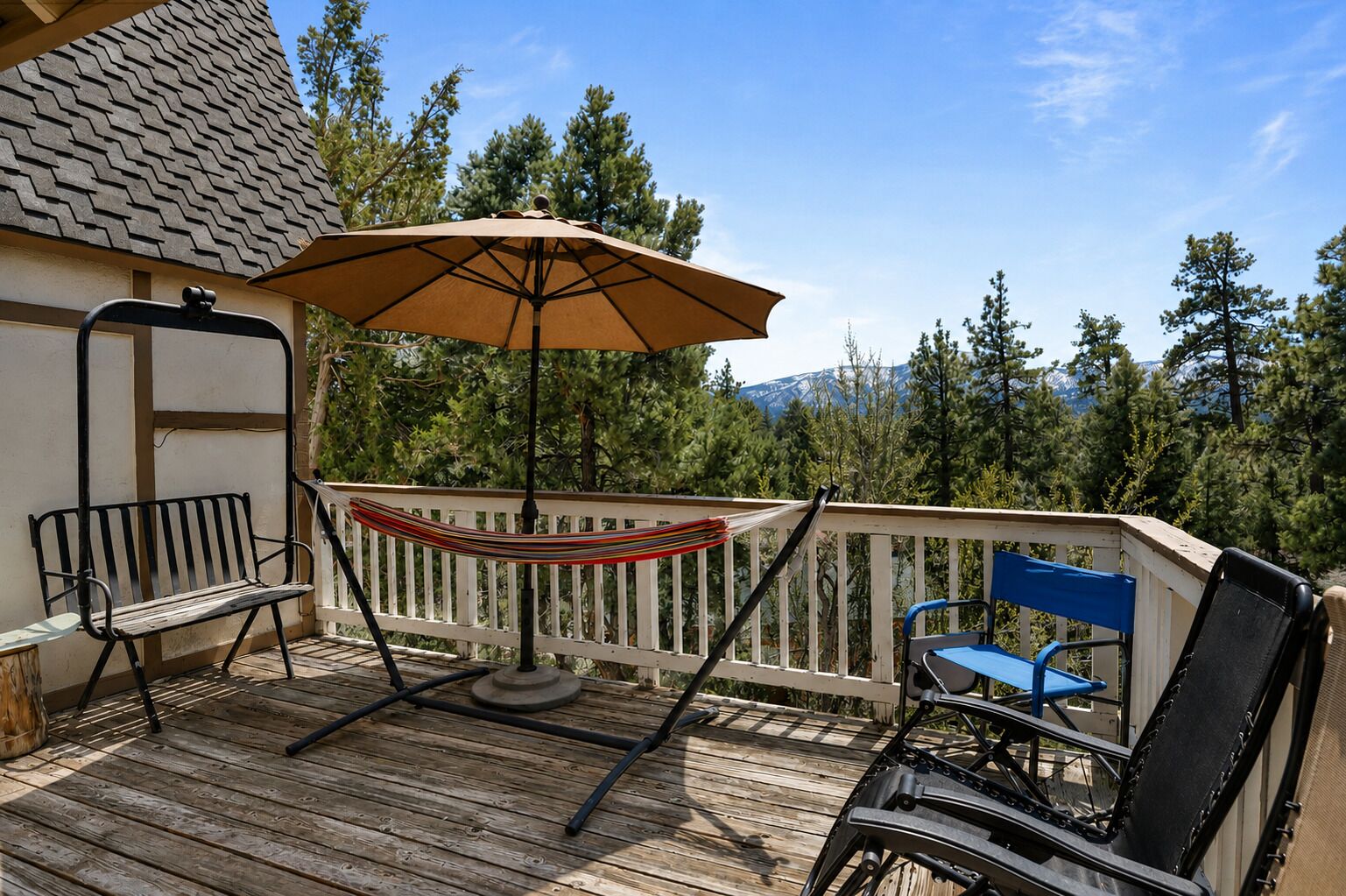 A wooden deck with a hammock, a table with an umbrella, and two chairs.