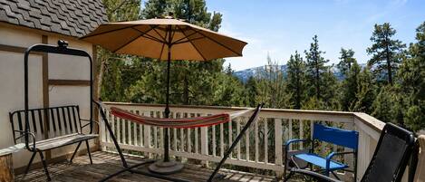 A wooden deck with a hammock, a table with an umbrella, and two chairs.
