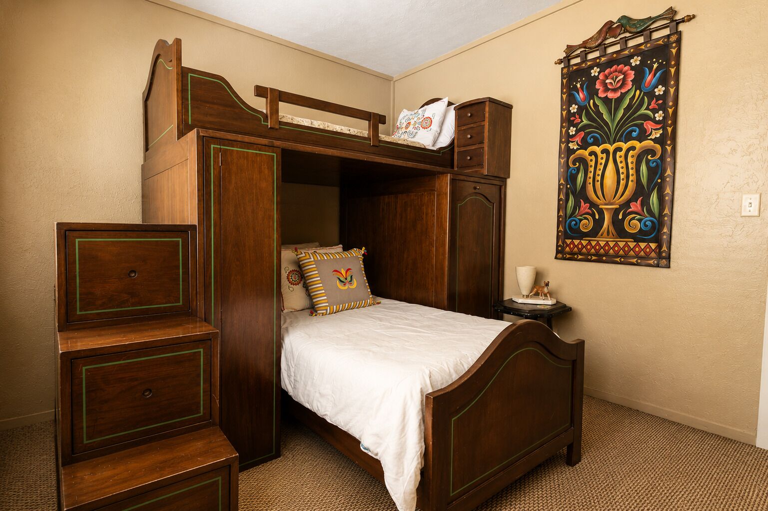 Een slaapkamer met een stapelbed, een dressoir, een nachtkastje en een decoratief wandtapijt.