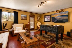 A cozy room with a sofa, a wooden table, a foosball table, a mounted deer head, and a large TV on the wall. - Antelope Retreat (Big Bear City)