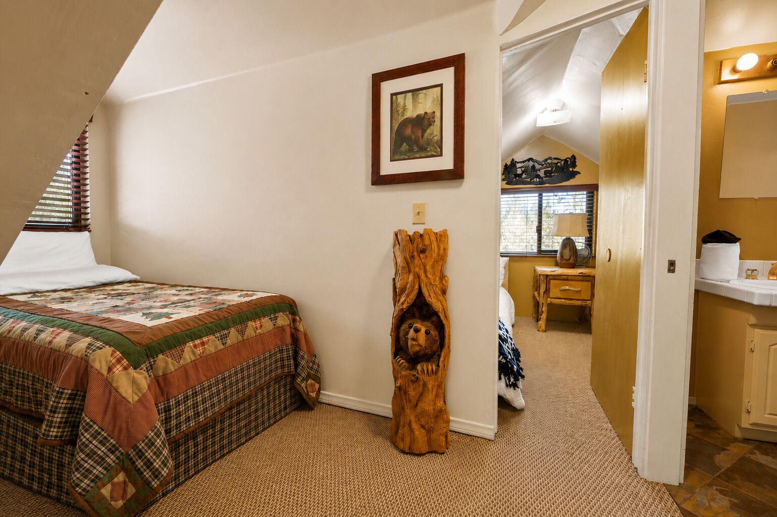 Ein Schlafzimmer mit einem Bett, einer Holzskulptur, einem Gemälde und einem durchgegangenen Tür sichtbaren Badezimmer.