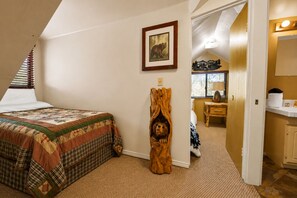 A bedroom with a bed, a wooden sculpture, a painting, and a bathroom visible through an open door. - Antelope Retreat (Big Bear City)