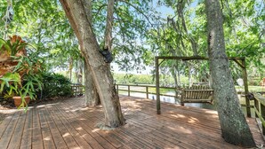 A wooden deck with a wooden swing set and a pond in the background. - STUNNING WATERFRONT RETREAT!!! (Lake Panasoffkee)