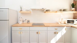 A modern kitchen with white cabinetry, a wooden countertop, a coffee machine, a microwave, and a brick wall. - Airy Midcentury Loft Apartment in SoMa (Little Rock)