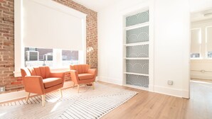 A modern living room with a brick wall, two orange armchairs, a patterned rug, and a built-in shelving unit with geometric designs. - Airy Midcentury Loft Apartment in SoMa (Little Rock)