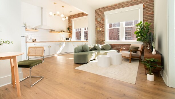 A modern living room with a green sofa, wooden coffee table, and a dining area with a wooden table and chairs. - Airy Midcentury Loft Apartment in SoMa (Little Rock)