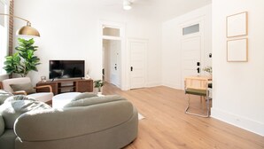A modern living room with a flat-screen TV, a green sofa, a wooden coffee table, and a potted plant. - Airy Midcentury Loft Apartment in SoMa (Little Rock)