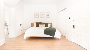 A spacious bedroom with a large bed, white walls, and a wooden floor. There are three framed pictures on the wall and a door on the right. - Airy Midcentury Loft Apartment in SoMa (Little Rock)