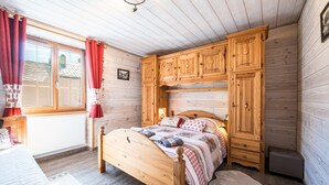 Una camera da letto con pannelli in legno, un letto, armadi a muro, una finestra con tende e un termosifone.