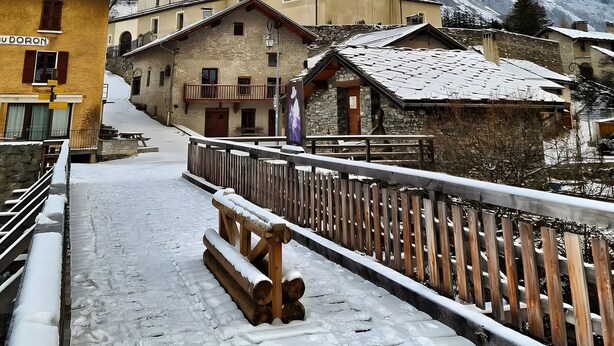 Un villaggio innevato con una chiesa, edifici in legno e montagne sullo sfondo.
