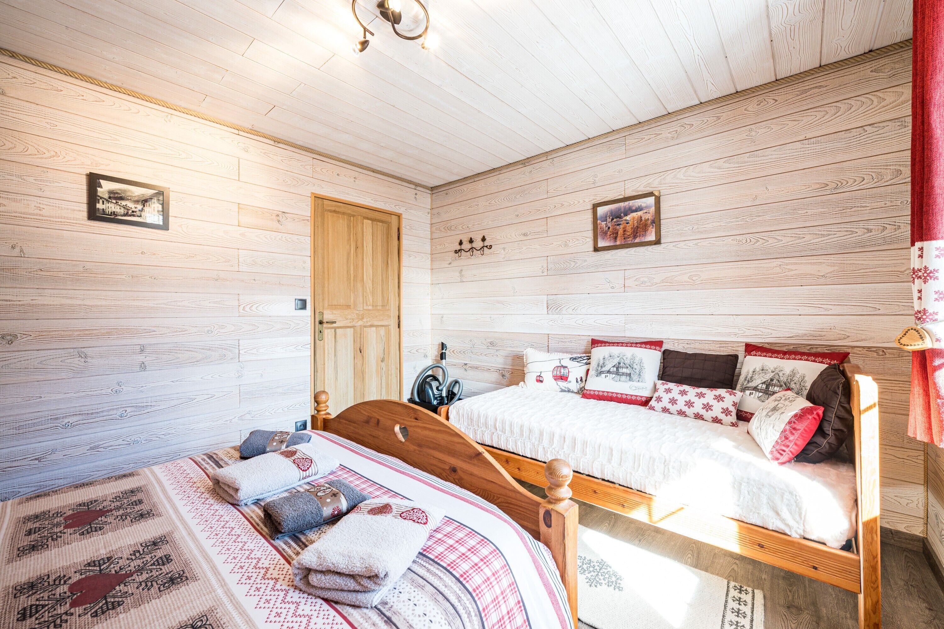 A wooden-paneled room with two beds, a wooden door, and two wall-mounted light fixtures.