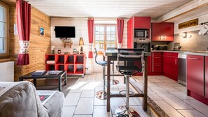 Una cucina compatta con zona pranzo, pareti in legno e una TV montata sopra il bancone.