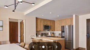 A modern kitchen with wooden cabinets, a stainless steel refrigerator, and a central island with bar stools. - Fabulous luxury resort hotel suite in delightful Avon w/ AC, WiFi, fitness, pool (Avon)