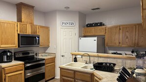 A kitchen with wooden cabinets, a microwave, stove, sink, and a refrigerator. - Backyard Oasis in Brownsville! (Brownsville)