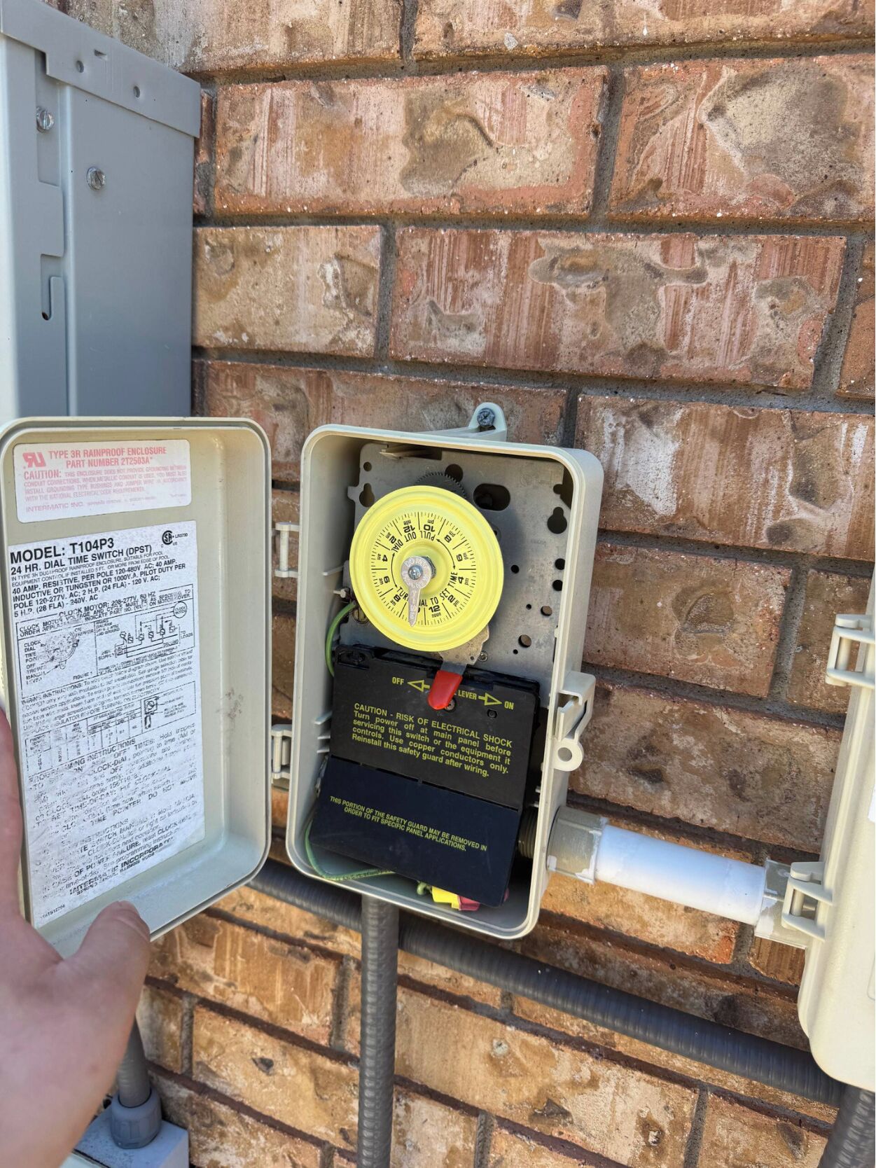 A utility box with a dial switch and a manual on it, mounted on a brick wall.