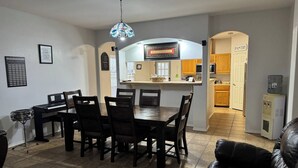 A dining area with a piano, a dining table with chairs, a black leather couch, and a kitchen in the background. - Backyard Oasis in Brownsville! (Brownsville)