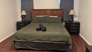 A neatly arranged bedroom with a large bed, two bedside tables with lamps, and a window with a curtain. - Backyard Oasis in Brownsville! (Brownsville)