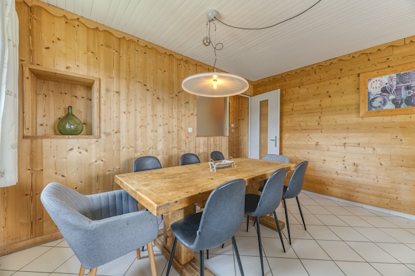 Una habitación con paneles de madera, una mesa de madera y seis sillas, una lámpara colgante y una obra de arte enmarcada en la pared.