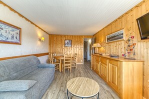 Una habitación acogedora con sofá, una mesa de comedor y una zona de cocina con armarios de madera y televisor.