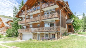A multi-story wooden chalet with balconies, a stone base, and a clear sky.