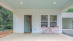 A covered porch with a green door, two folding chairs, and a wreath on the door.