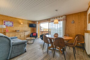Ein Holzinnenraum mit einer Couch, einem Esstisch, Stühlen, einem Fernseher und einem Fenster mit Blick.