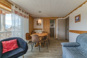 Ein Zimmer mit Holzboden, einem Esstisch mit Stühlen, einer Couch und Bergblick durch das Fenster.