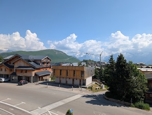 Un edificio con fachada de madera y un balcón, un estacionamiento y un paisaje montañoso al fondo.