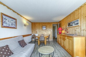Une pièce chaleureuse avec un mur en bois, une table à manger avec des chaises, une petite table ronde et un canapé agrémenté de coussins à motifs.