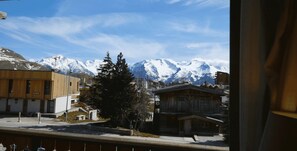 Vista de un pueblo con montañas nevadas al fondo, un edificio de madera en primer plano y un edificio moderno con techo inclinado.