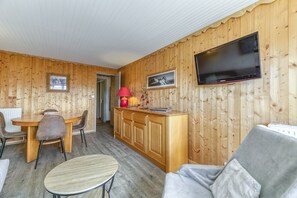 Une pièce aux murs lambrés, comprenant une table à manger, des chaises, un canapé, un téléviseur et un meuble.