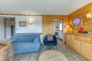 A room with a blue sofa, a wooden cabinet, and a chair with a patterned cushion. - Apartment 'Les Crocus 1-2' with Balcony and Wi-Fi (Huez)