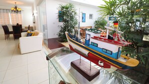 A model ship in a glass display case, surrounded by indoor plants and furniture in a modern living space.