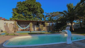 A swimming pool with a waterfall feature, surrounded by a patio with lounge chairs and a hammock.