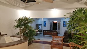 A spacious living area with a ceiling fan, a wooden bench, a coffee table, and potted plants.