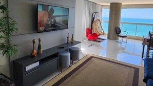A modern living room with a flat-screen TV, a hanging chair, and a view of the ocean. - 04 BEDROOMS FACING THE SEA WITH AIR CONDITIONING IN TWO SUITES (Praia do Morro Guarapari)