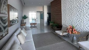 A modern living room with a grey sofa, a coffee table, and a decorative wall panel. - 04 BEDROOMS FACING THE SEA WITH AIR CONDITIONING IN TWO SUITES (Praia do Morro Guarapari)