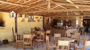 A rustic dining area with wooden chairs and tables, a brick wall, and a wooden ceiling.