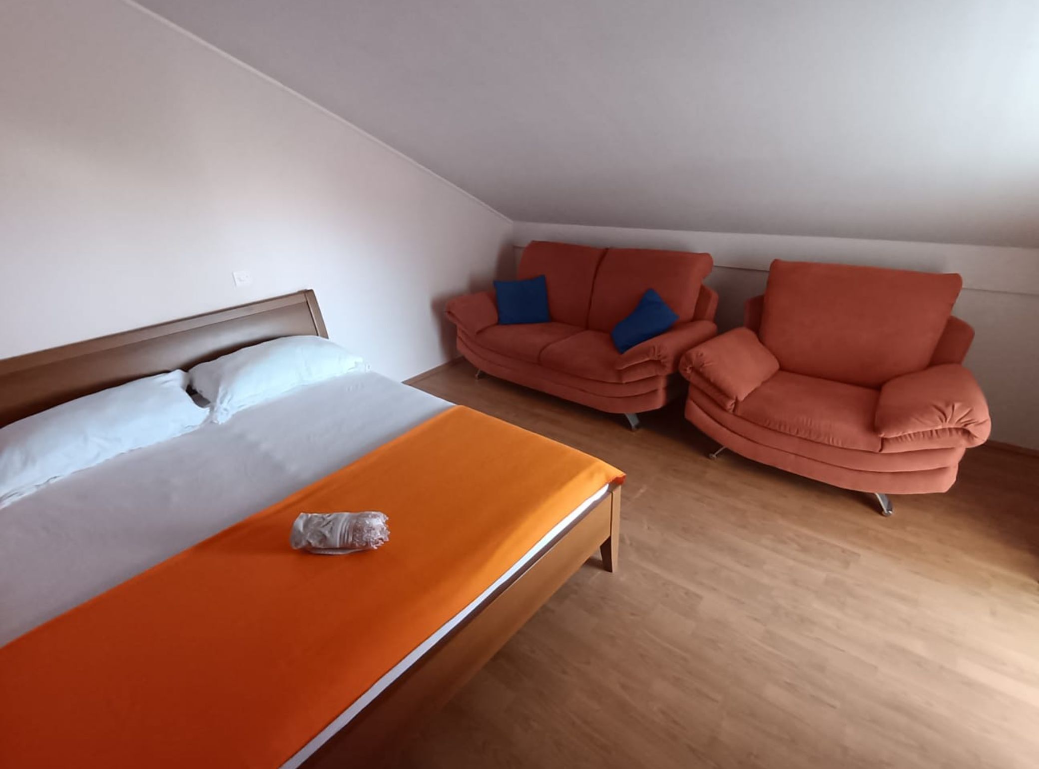A bedroom with a bed, an orange blanket, two sofas, and a chair.