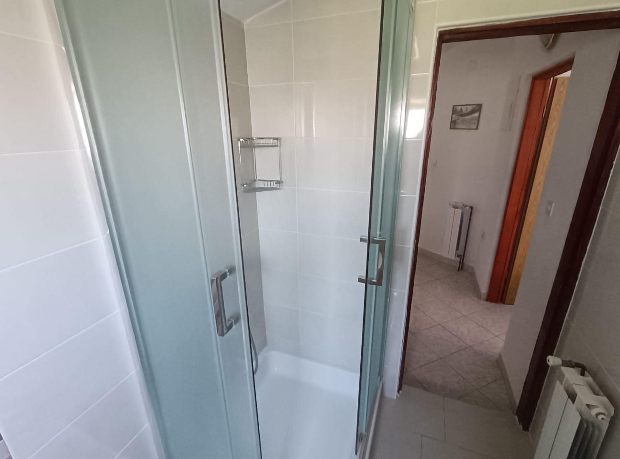 Une salle de bain avec une douche à parois de verre, des carreaux blancs et un porte-serviettes apparent.