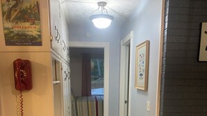 Een smalle gang met een telefoon aan de linkerkant, een kamerbreed tapijt op de vloer en een deur die leidt naar een slaapkamer.