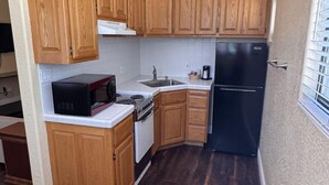 A compact kitchen with wooden cabinets, a black refrigerator, a stove, and a microwave.