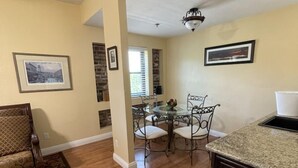 Un salón espacioso con piso de madera, un mueble de madera oscura, una mesa de comedor de vidrio con cuatro sillas y una alfombra estampada.