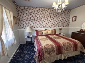 Une chambre à coucher avec un papier peint à motifs floraux, un grand lit recouvert d’une couvre-lit à motifs, un lustre et une table de chevet avec une lampe.